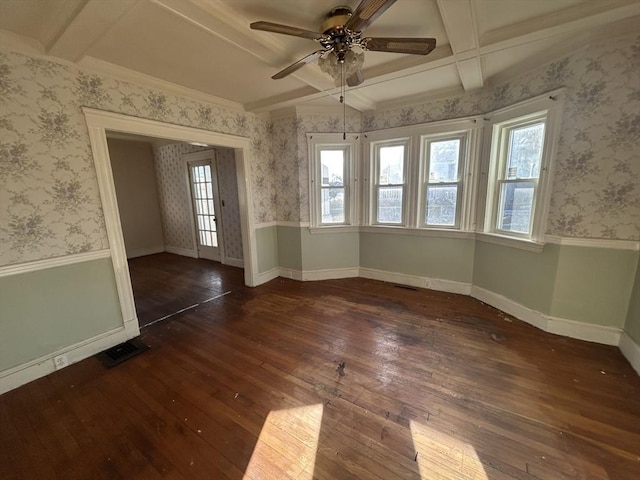 empty room with beamed ceiling, a wealth of natural light, ceiling fan, and dark hardwood / wood-style flooring