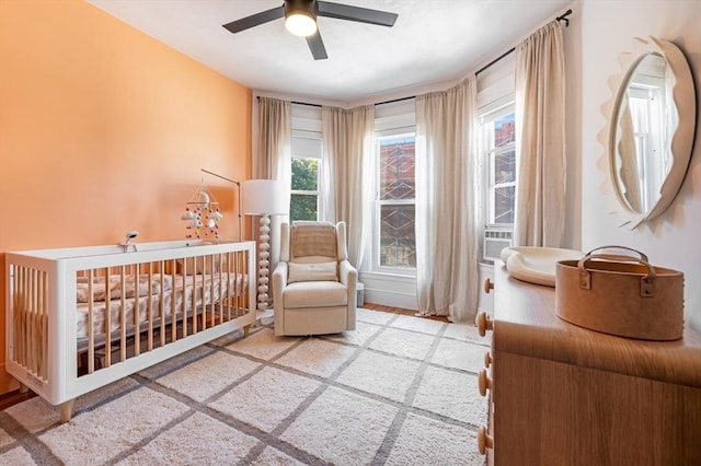 bedroom with a ceiling fan, a nursery area, and multiple windows
