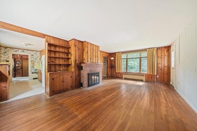 36 Grove St, Hanover, MA 02339 - unfurnished living room with radiator, hardwood / wood-style flooring, a brick fireplace, and wood walls