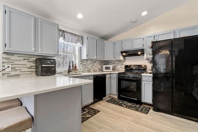 kitchen featuring vaulted ceiling, black appliances, sink, a kitchen breakfast bar, and kitchen peninsula