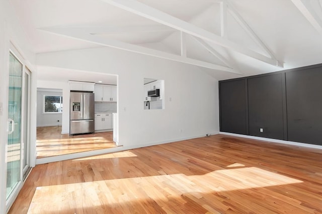 unfurnished living room with light hardwood / wood-style flooring and vaulted ceiling with beams