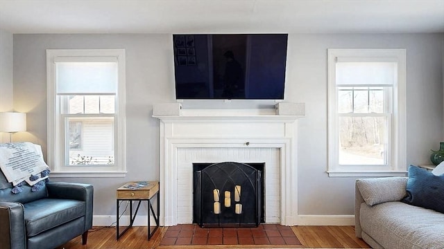 living area featuring a brick fireplace, wood finished floors, and baseboards