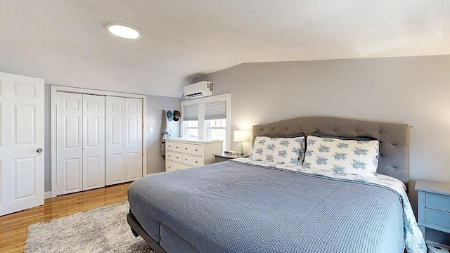 bedroom with vaulted ceiling, a closet, a wall mounted AC, and wood finished floors