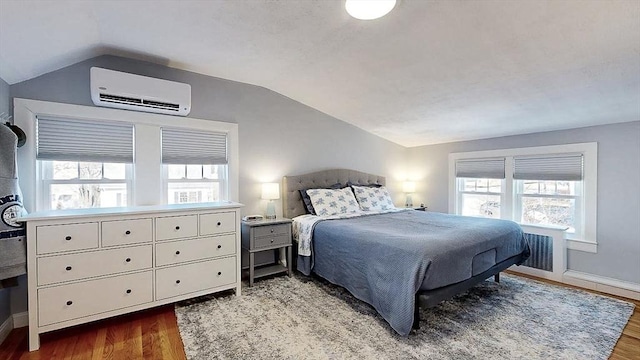 bedroom featuring vaulted ceiling, an AC wall unit, wood finished floors, and baseboards