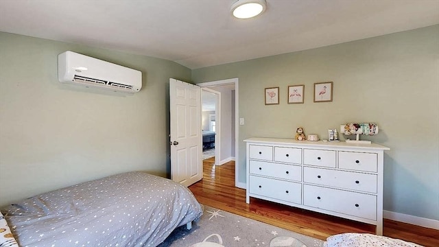 bedroom featuring wood finished floors, baseboards, and a wall mounted AC