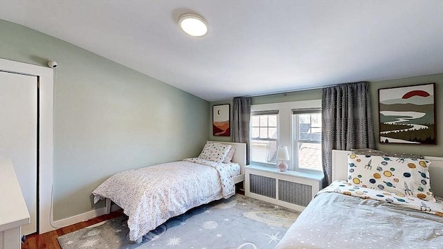 bedroom with lofted ceiling, baseboards, wood finished floors, and radiator