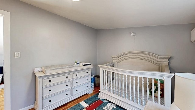 bedroom featuring a nursery area, baseboards, and wood finished floors