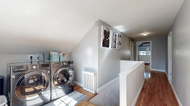 clothes washing area featuring radiator heating unit, baseboards, washing machine and clothes dryer, and wood finished floors