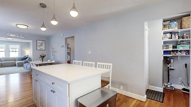 kitchen with a kitchen island, wood finished floors, white cabinetry, light countertops, and decorative light fixtures