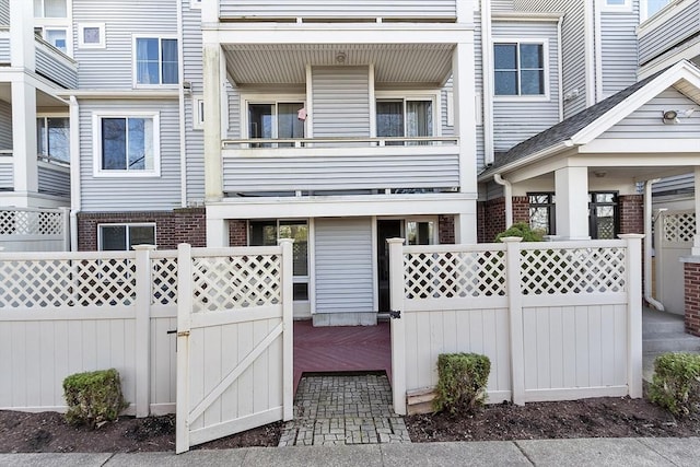 multi unit property with a gate, brick siding, fence, and a balcony