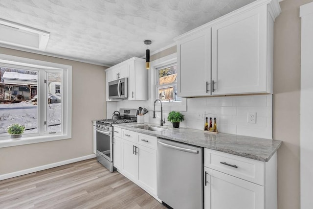 kitchen featuring sink, white cabinetry, light hardwood / wood-style flooring, stainless steel appliances, and light stone countertops