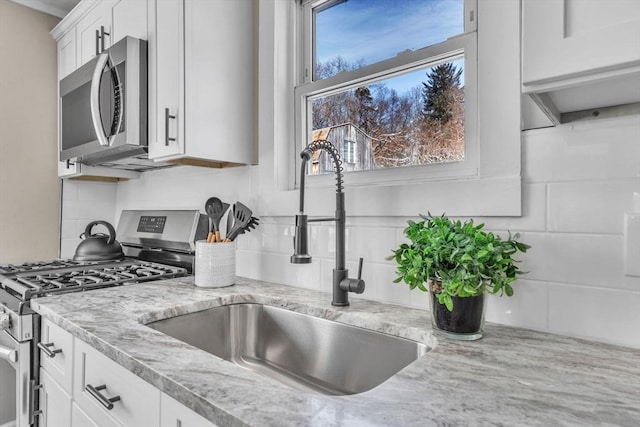 kitchen featuring sink, light stone counters, tasteful backsplash, appliances with stainless steel finishes, and white cabinets