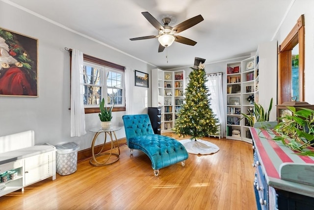 sitting room featuring ceiling fan, baseboards, wood finished floors, and crown molding