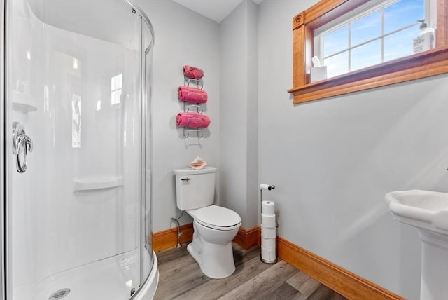 bathroom featuring baseboards, wood finished floors, toilet, and a stall shower