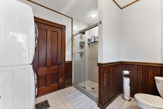 full bathroom featuring tile patterned floors, a wainscoted wall, stacked washer and dryer, and a stall shower