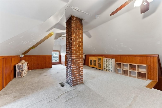 additional living space featuring visible vents, a ceiling fan, wood walls, decorative columns, and vaulted ceiling