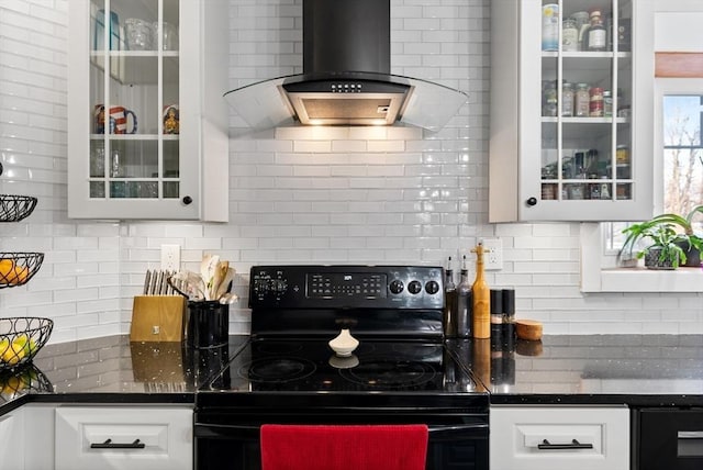 kitchen featuring glass insert cabinets, white cabinetry, wall chimney range hood, black electric range oven, and backsplash