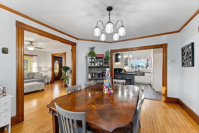 dining space featuring ceiling fan with notable chandelier, baseboards, crown molding, and light wood-style floors