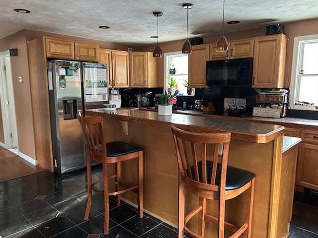 kitchen with stainless steel fridge with ice dispenser, a healthy amount of sunlight, hanging light fixtures, and a kitchen breakfast bar