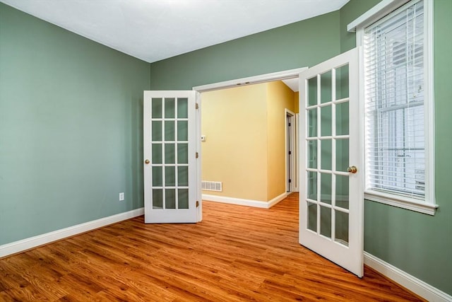 empty room featuring a wealth of natural light, french doors, visible vents, and wood finished floors