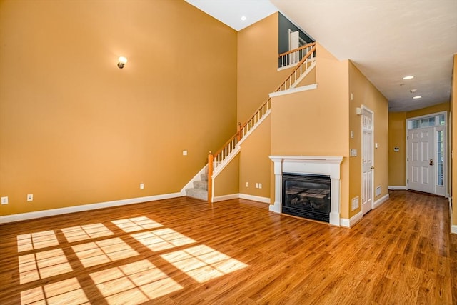 unfurnished living room with stairway, baseboards, and wood finished floors