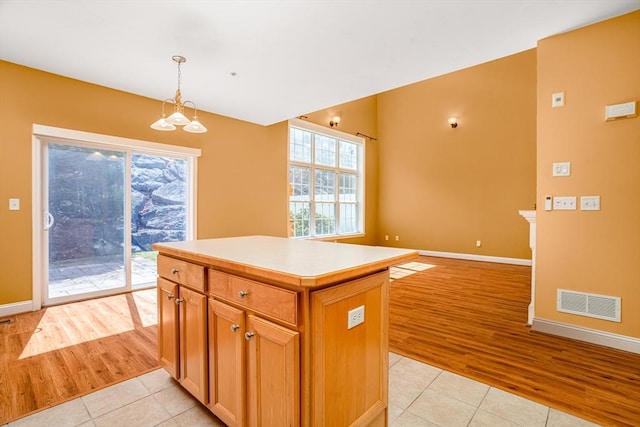 kitchen with light countertops, a kitchen island, light tile patterned flooring, visible vents, and hanging light fixtures