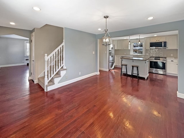 kitchen featuring decorative backsplash, stainless steel appliances, dark wood finished floors, and a kitchen breakfast bar