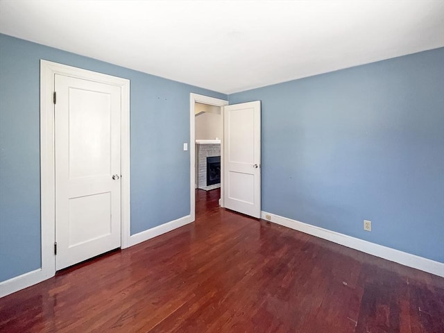 unfurnished bedroom with a brick fireplace, baseboards, and wood finished floors