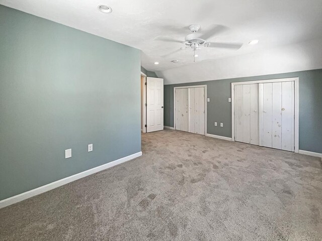 unfurnished bedroom with lofted ceiling, baseboards, and two closets