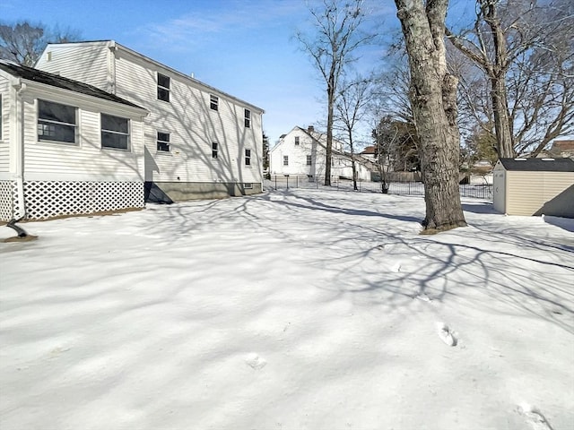 yard layered in snow featuring a storage shed, fence, and an outbuilding