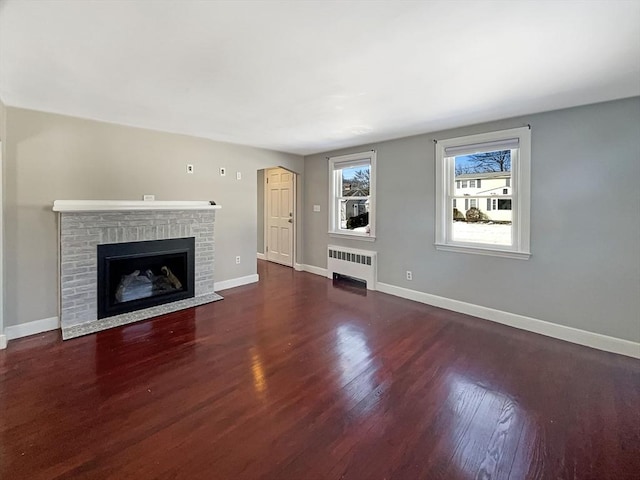 unfurnished living room featuring baseboards, a brick fireplace, wood finished floors, and radiator