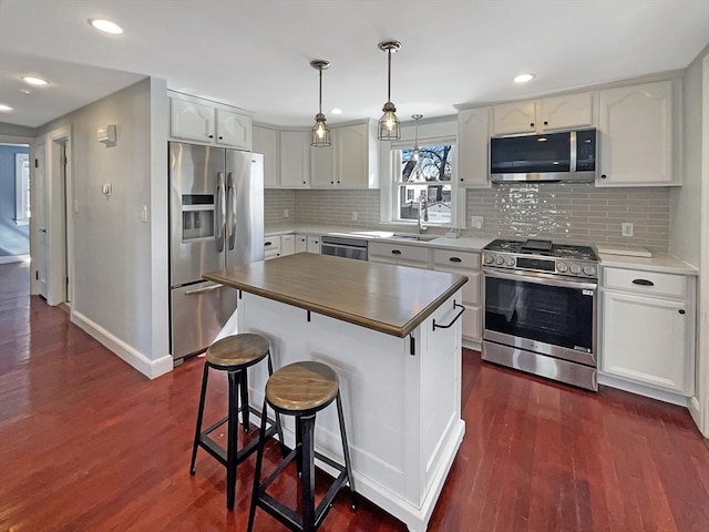 kitchen featuring a breakfast bar, dark wood finished floors, stainless steel appliances, backsplash, and white cabinetry