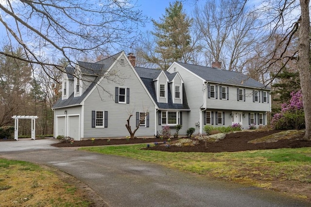 view of front facade featuring an attached garage, a shingled roof, driveway, and a chimney