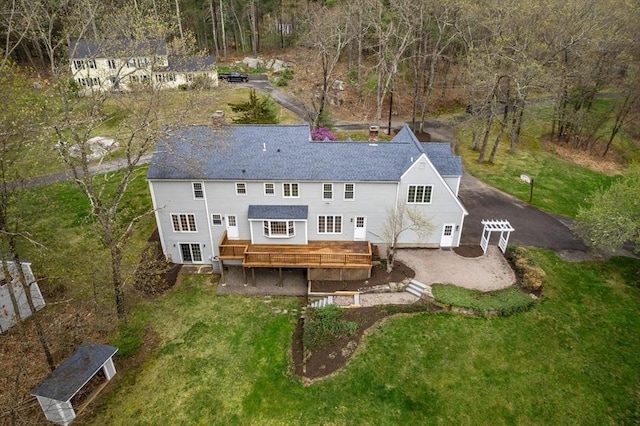 rear view of house featuring roof with shingles, a deck, a chimney, a patio area, and a yard