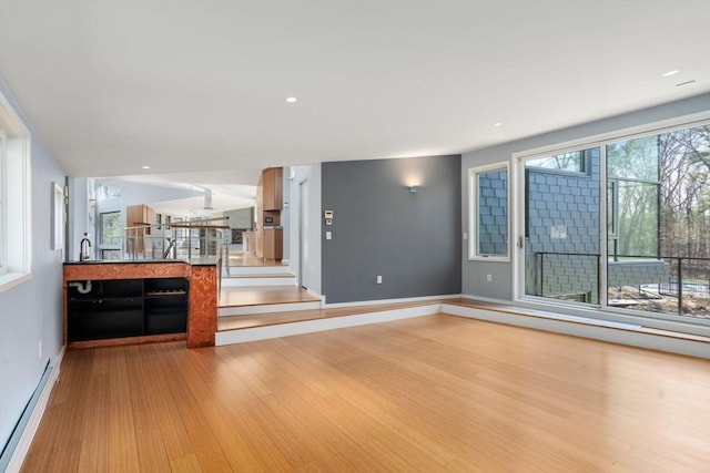 unfurnished living room featuring baseboards, wood finished floors, a baseboard heating unit, a sink, and recessed lighting