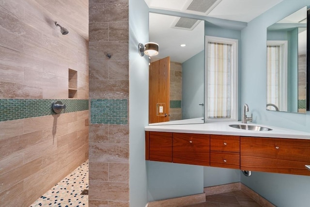full bath featuring vanity, a tile shower, and visible vents