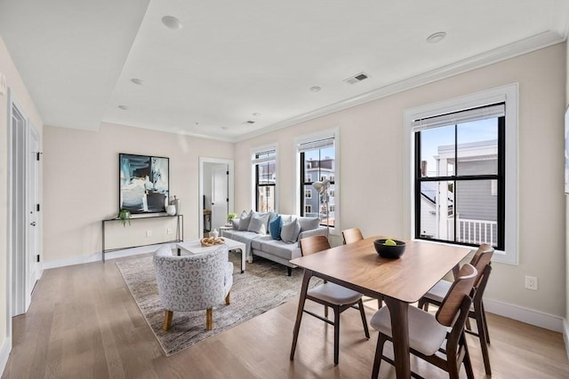 dining space with a healthy amount of sunlight, ornamental molding, and light hardwood / wood-style flooring