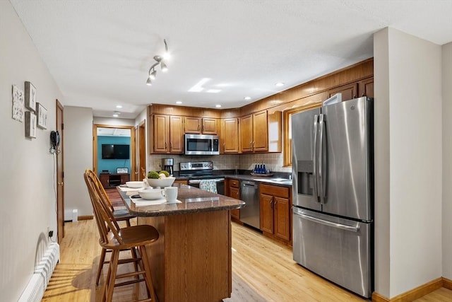 65 Martin Rd, Tewksbury, MA 01876 - kitchen with stainless steel appliances, light wood-style flooring, tasteful backsplash, brown cabinetry, and a center island