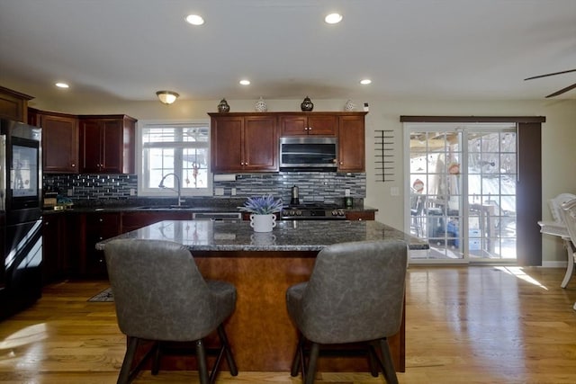 kitchen featuring reddish brown cabinets, a center island, light wood finished floors, stainless steel appliances, and a sink