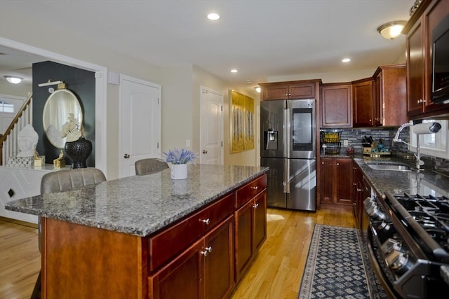 kitchen featuring black gas range oven, stainless steel fridge, dark brown cabinets, and a sink