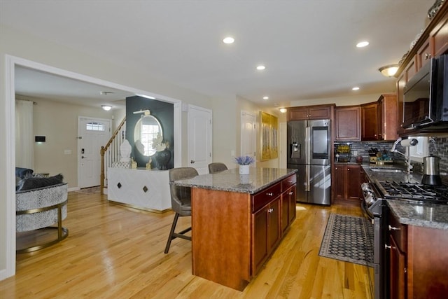 kitchen featuring reddish brown cabinets, a breakfast bar area, stainless steel appliances, light wood-style floors, and a sink