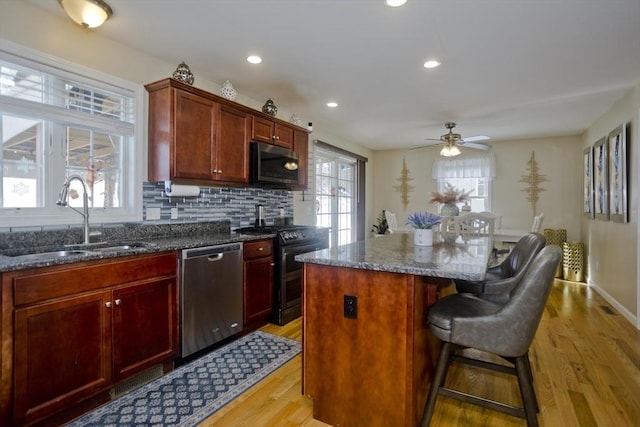 kitchen with reddish brown cabinets, a kitchen island, appliances with stainless steel finishes, a sink, and backsplash