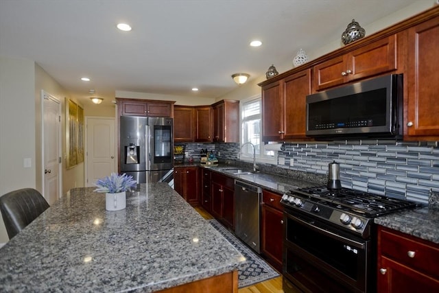 kitchen with decorative backsplash, dark stone counters, stainless steel appliances, a sink, and recessed lighting