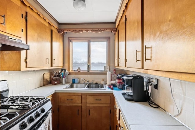 kitchen featuring under cabinet range hood, a sink, light countertops, decorative backsplash, and gas stove