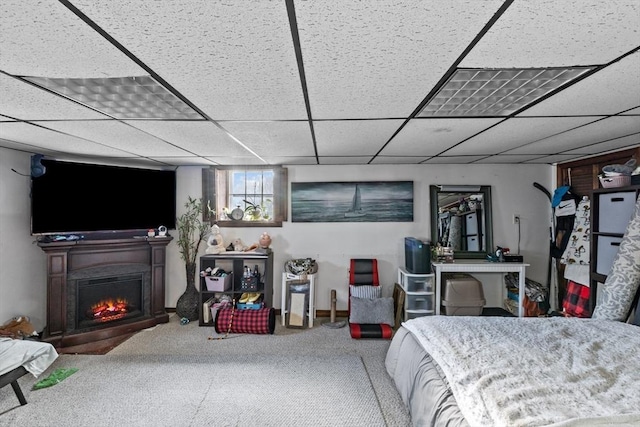 carpeted bedroom featuring a paneled ceiling and a warm lit fireplace