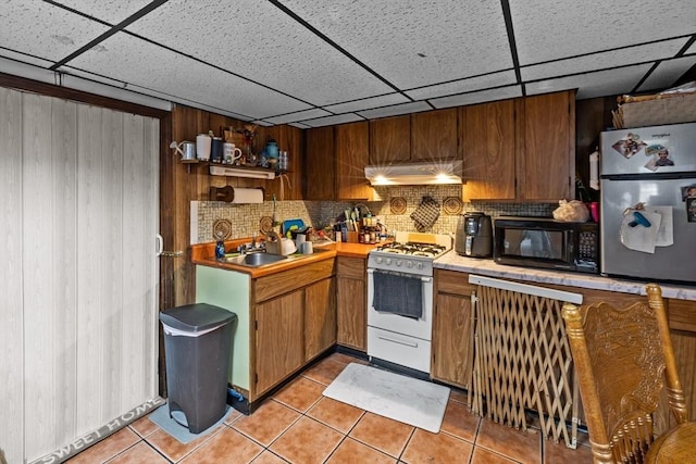 kitchen featuring black microwave, light tile patterned flooring, under cabinet range hood, backsplash, and gas range gas stove