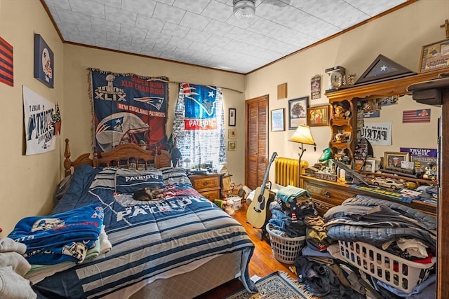 bedroom featuring ornamental molding, a closet, radiator heating unit, and wood finished floors