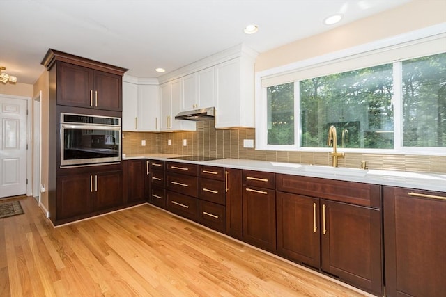 113 Sparrow Rd, Stoughton, MA 02072 - kitchen featuring stainless steel oven, under cabinet range hood, white cabinets, backsplash, and light wood-style floors