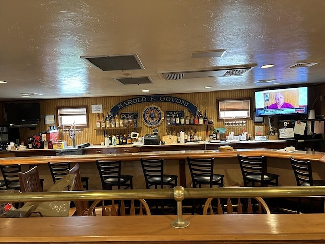 bar featuring a dry bar, wood walls, visible vents, and a textured ceiling