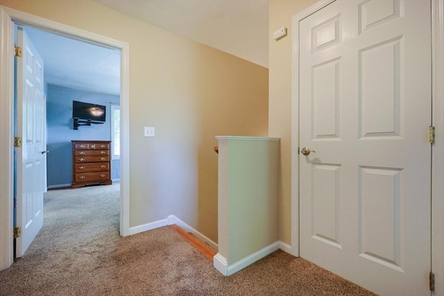 hallway featuring carpet floors, baseboards, and an upstairs landing